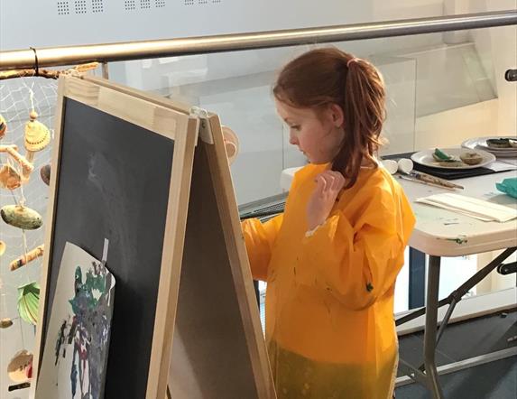 Girl at a craft workshop, painting at an art easel