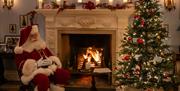 Santa sitting beside a large marble fireplace and Christmas tree