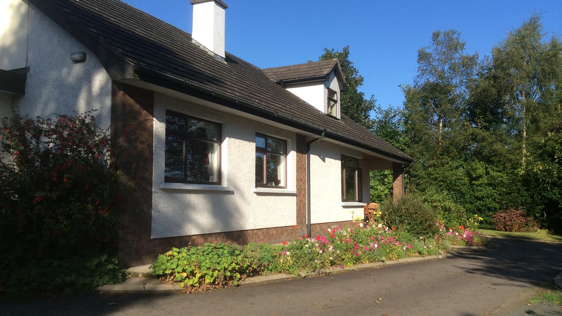 Image of a cream bungalow with flower beds and tress surrounding it