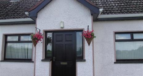 Image of the front of a white bungalow with flower baskets hanging on either side of the door