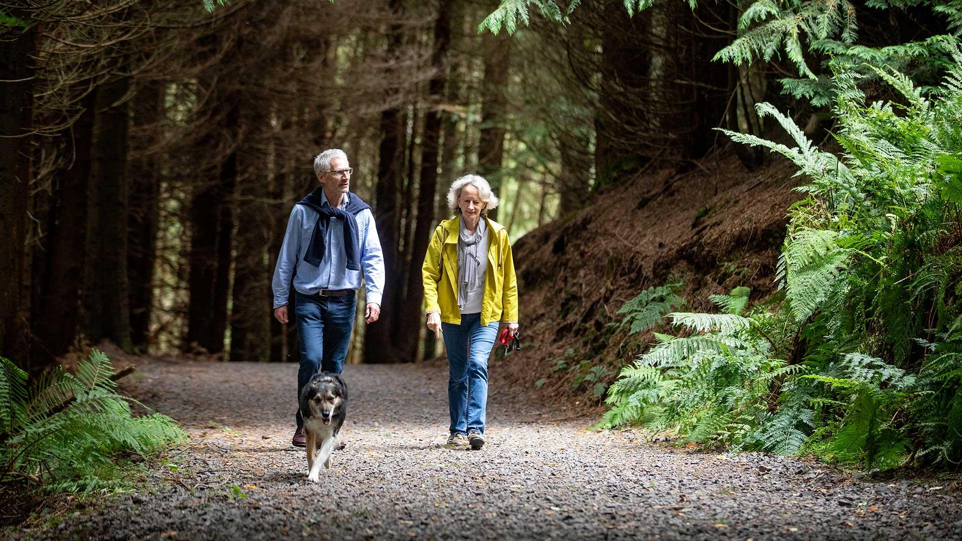 A couple walking through a forest path with their dog