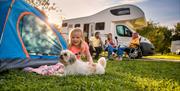 Girl with dog sitting outside tent with family in background outside motorhome
