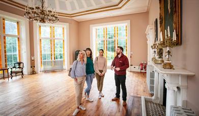 Three ladies stand with a tour guide inside the ballroom of Lissan House.