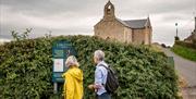 A mature couple looking at the Carleton trail sign with St Macartans (Forth) Chapel in the background