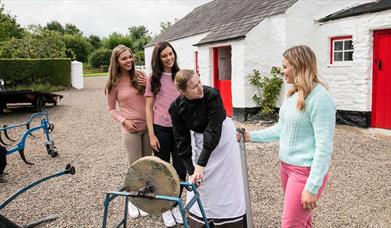 Girls pictured with a woman in period dress outside an old thatched cottage with a red door