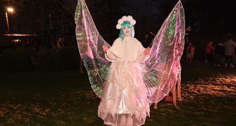 A woman dressed as a Christmas fairy is holding out her wings