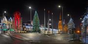 Magherafelt Christmas tree is in the centre of the panoramic image. It is night time and other Christmas lights are glowing in the background