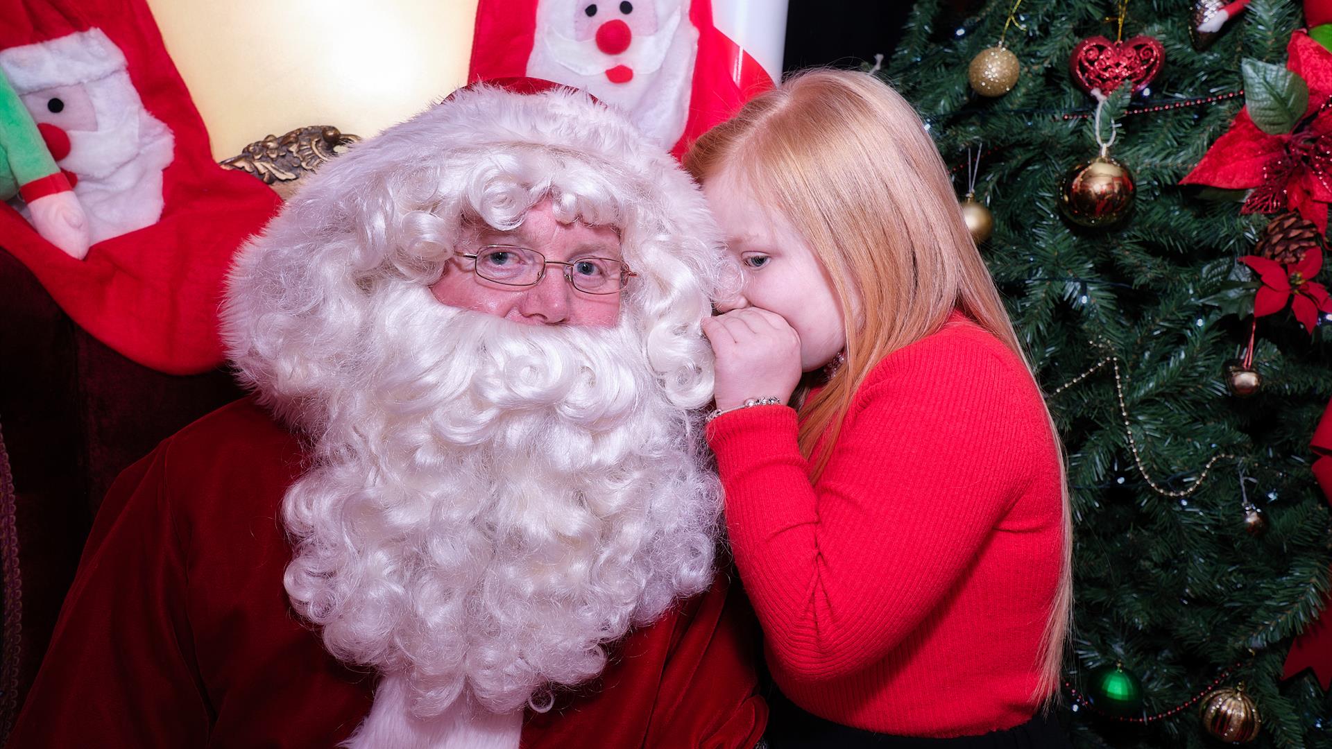 Young girl whispering in Santa's ear