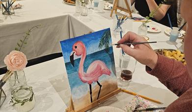H shaped table with people painting a pink flamingo