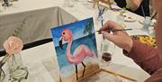 H shaped table with people painting a pink flamingo