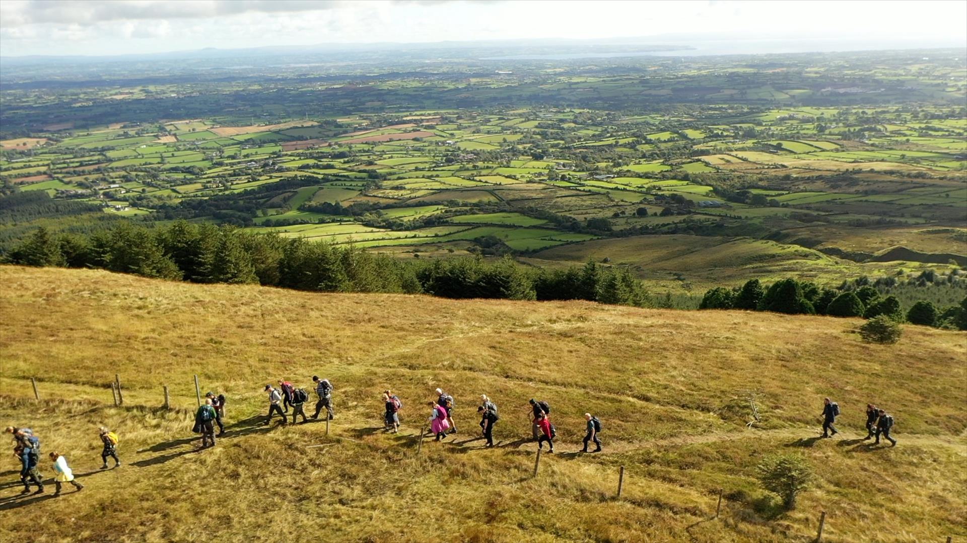 Drone image of walkers on Slieve Gallion with panoramic scenery stretching for miles and Lough Neagh in the far distance