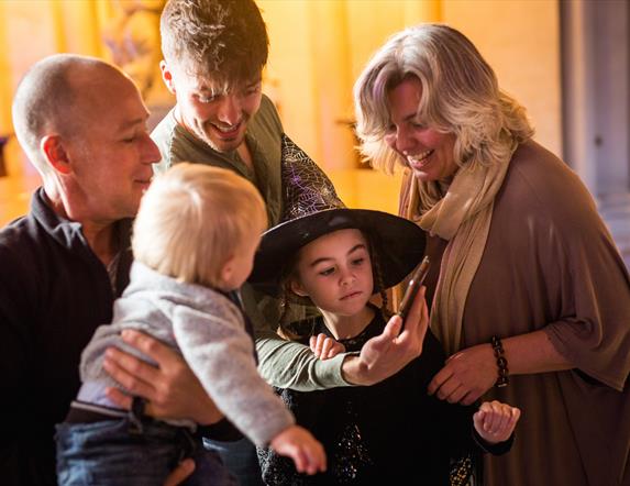 Girl dressed as witch with family, laughing at mobile phone.