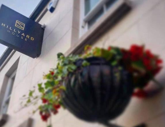 sign for Hillyard Huse on outside wall with hanging flower basket below.