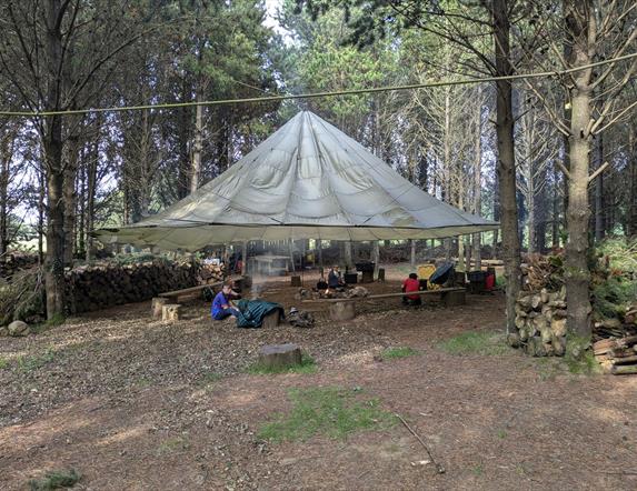 Men at Tepee in forest setting with campfire.