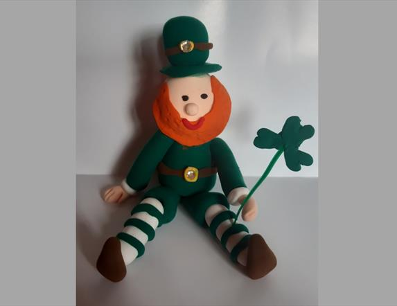 A handmade leprechaun with a shamrock in their hand, sitting on a table, on St Patrick's Day at Newry and Mourne Museum.