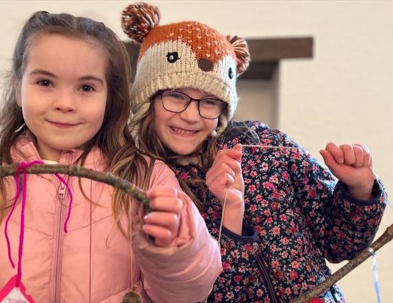 Two girls looking at the camera proudly displaying art they made at the Terrific Trees event.