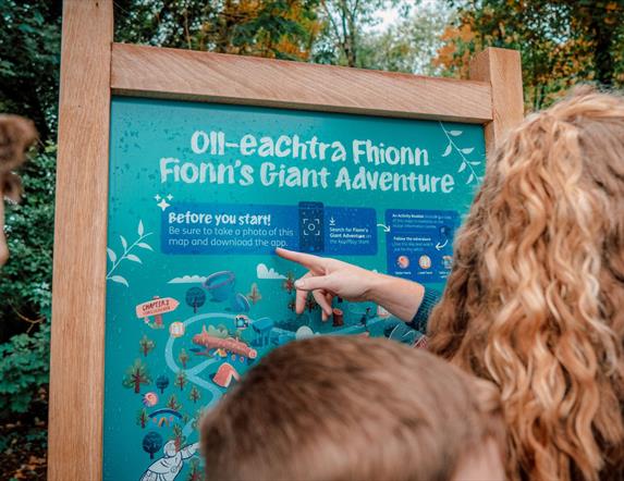 A family reading a sign at the entrance to Fionn's Giant Adventure  at Slieve Gullion Forest Park.