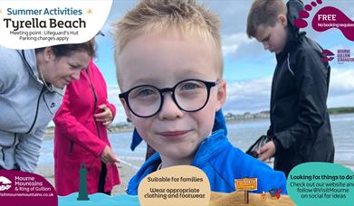 Upclose picture of a boy enjoying beach activities with three people in the background exploring a rock pool.