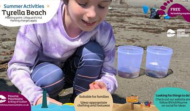 Girl looking closely at something she has found at the beach as part of the Beach Activities