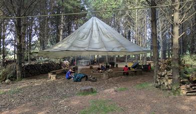 Men at Tepee in forest setting with campfire.