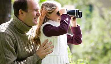 Two people bird watching in Castlewellan Forest Park. The child is looking through binoculars.