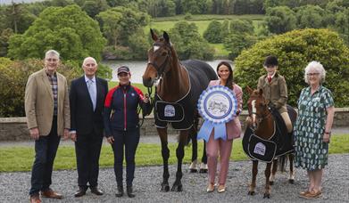 show organisers stand in front of castlewellan lake with a pony and a horse