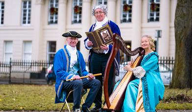 Three people in historical garments in front of a historical house.