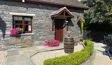 Front garden with paved path leading to the cottage's front door, decorated with flowers and a barrel.