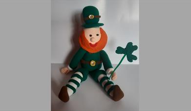 A handmade leprechaun with a shamrock in their hand, sitting on a table, on St Patrick's Day at Newry and Mourne Museum.