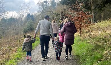 A family enjoying a walk in Slieve Gullion Forest Park. Two adults and two children holding hands, walking up a path together.