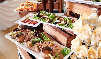 Buffet table with white plates on different tiers. Each has a colourful selection of food, pates, fresh figs, meats and charcuterie.