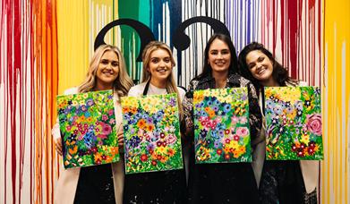 Image of group of girls holding paintings of flowers, painted in a class.