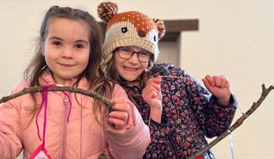 Two girls looking at the camera proudly displaying art they made at the Terrific Trees event.
