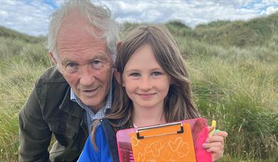 A child and and adult at beach activities at Tyrella Beach. Child holding a clipboard.