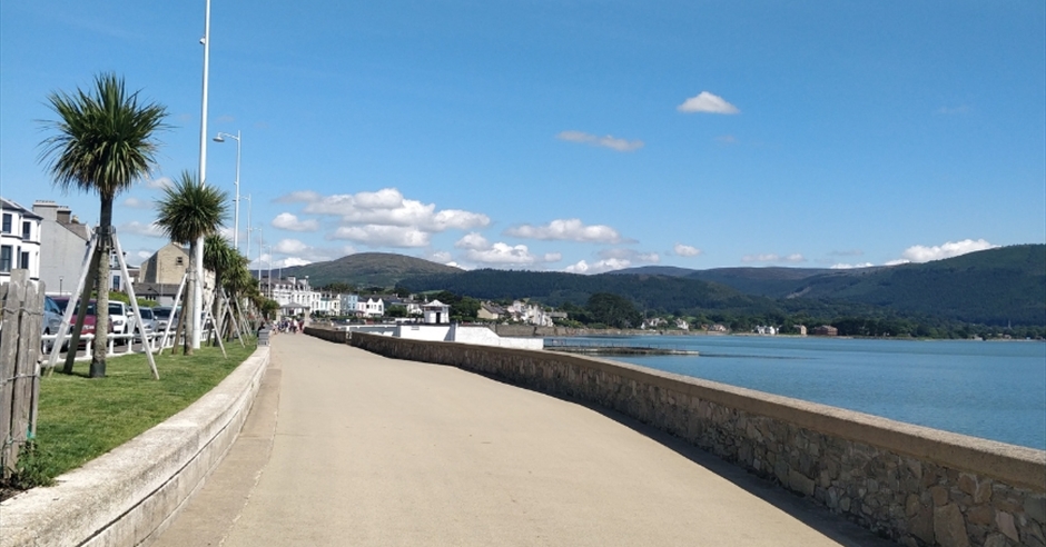 The bustling Promenade in Warrenpoint, Northern Ireland, featuring a bandstand, vibrant flowers, and views across Carlingford Lough to the Cooley Mountains.