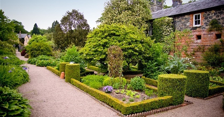 Saintfield, Downpatrick area, Northern Ireland: Lush green lawns and vibrant flower beds with a path winding through the cultivated gardens of Rowallane Garden, under a clear sky.