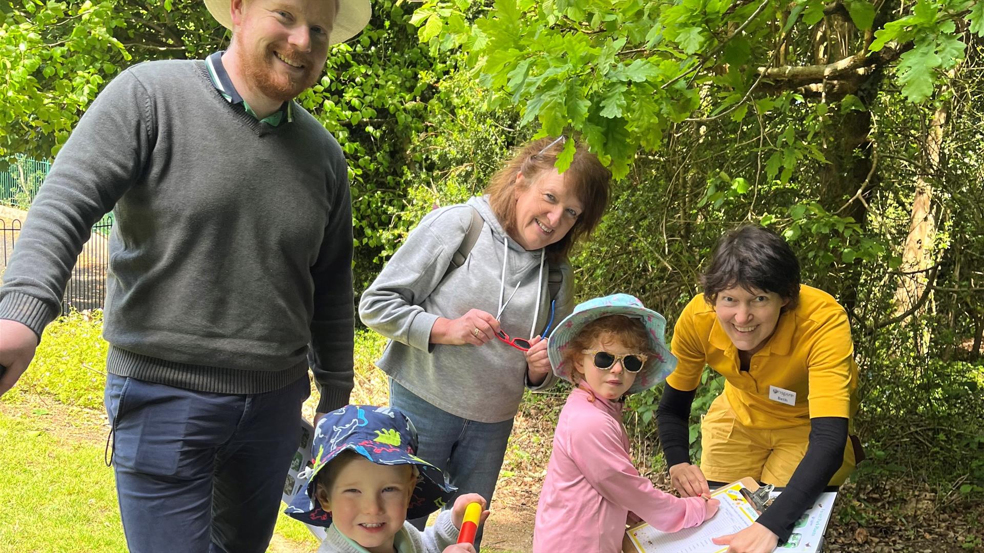 A group of five people gathered together, standing on gass, taking part in a family event and  a child is filling in answers to a clipboard.
