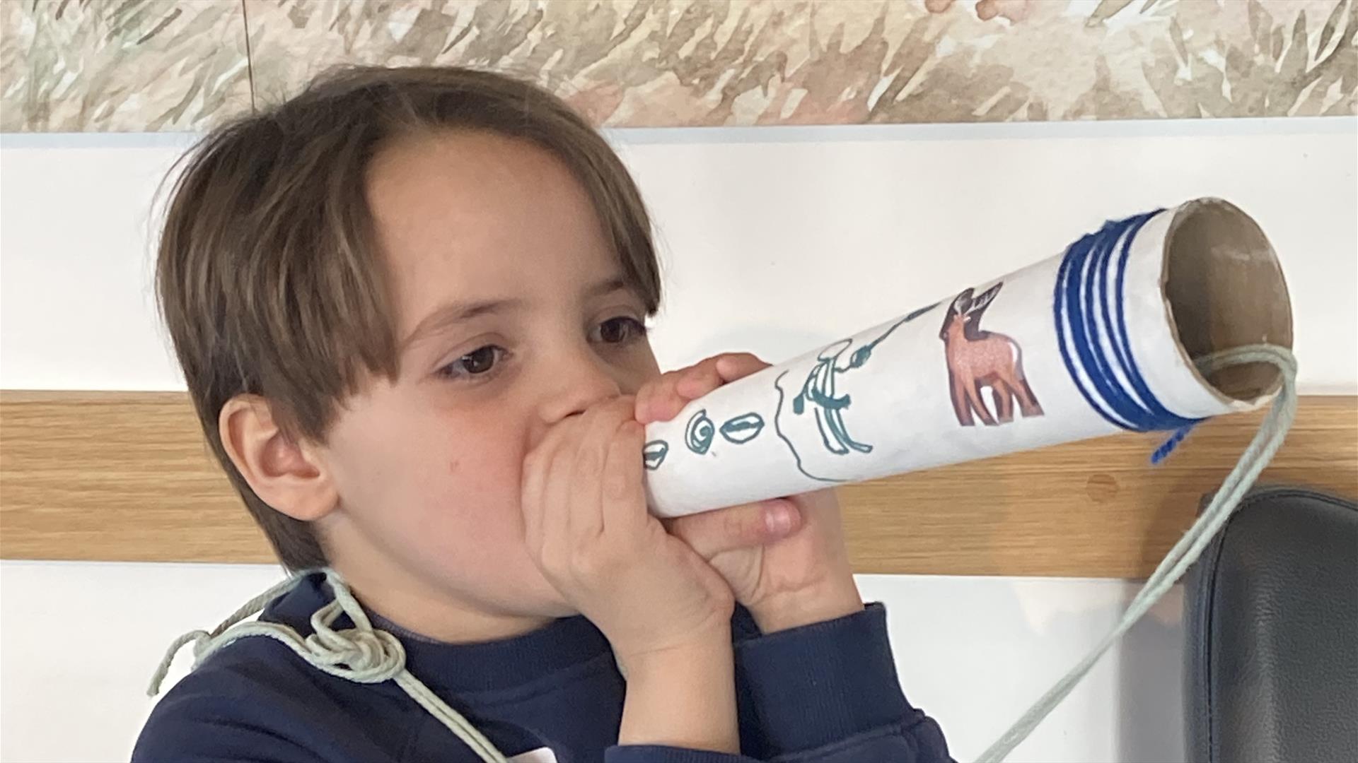 An image of a young boy demonstrating the use of the 'hunting horn' he made during one of the craft workshops.