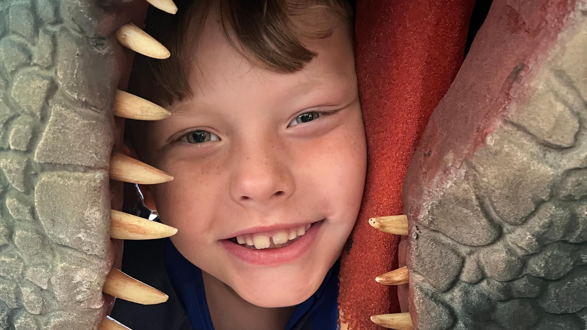 A boy gripped in the mouth of a dinosaur (dino not real)