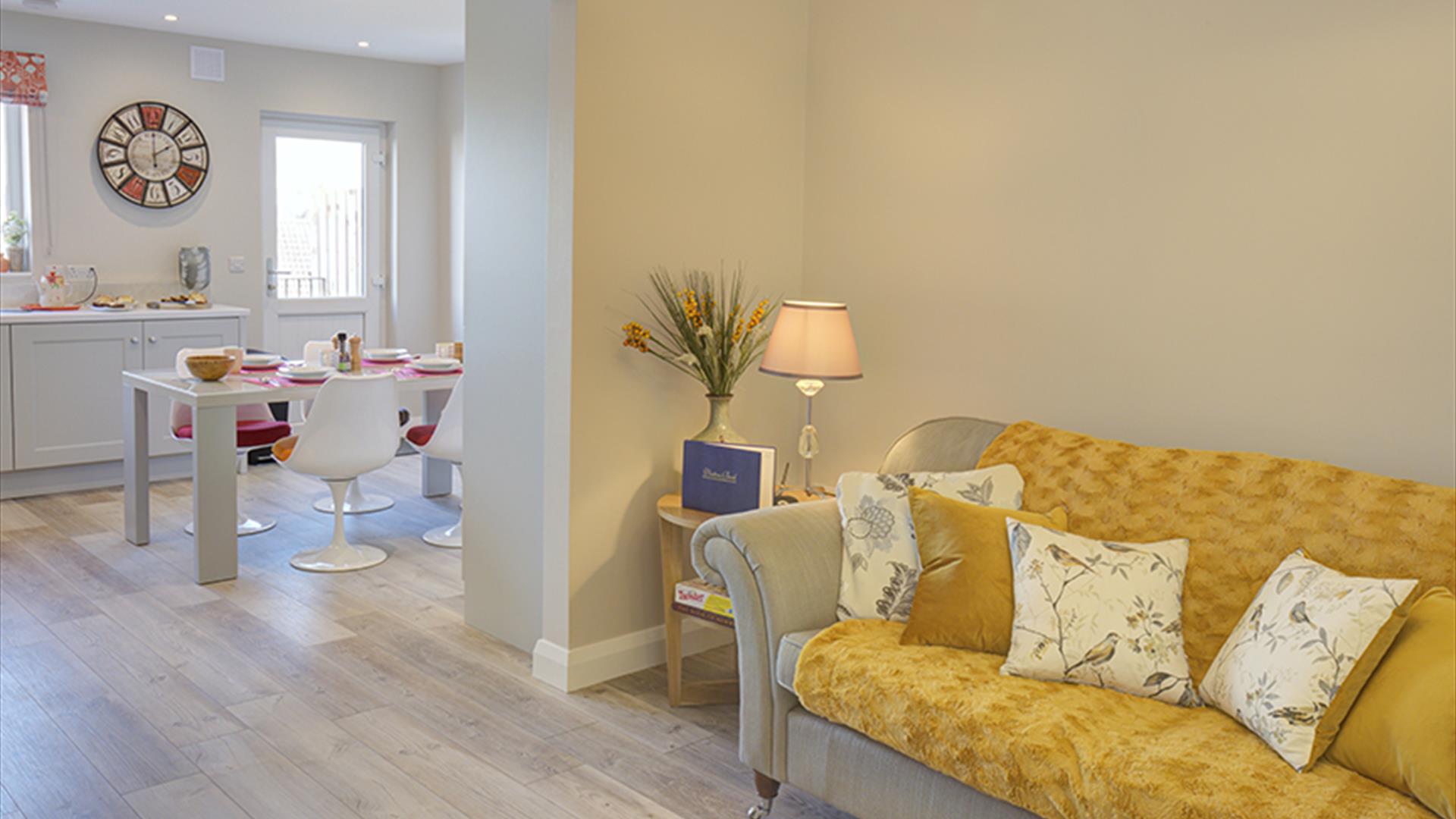 Open plan lounge area with a yellow sofa leading into a kitchen/dining room.