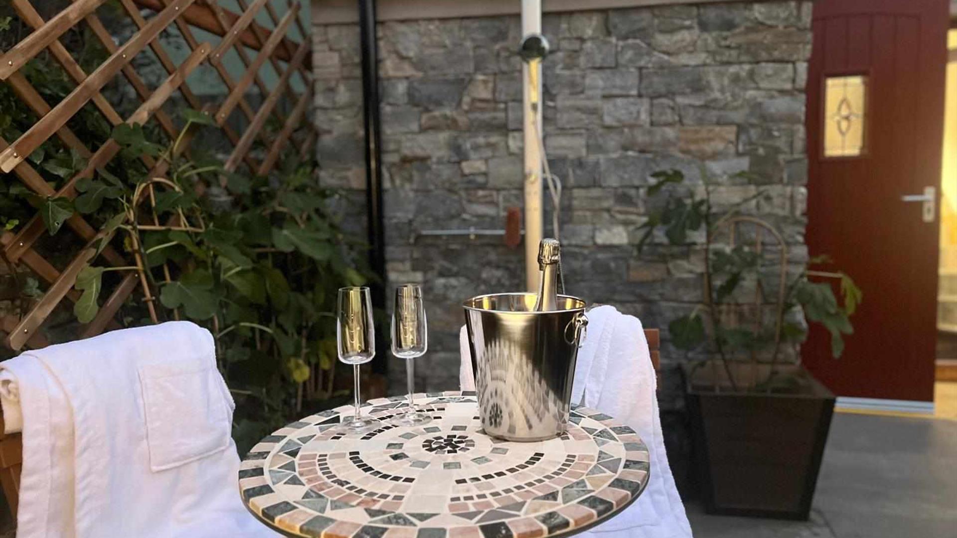 outdoor seating area with two glasses and a bottle of champagne