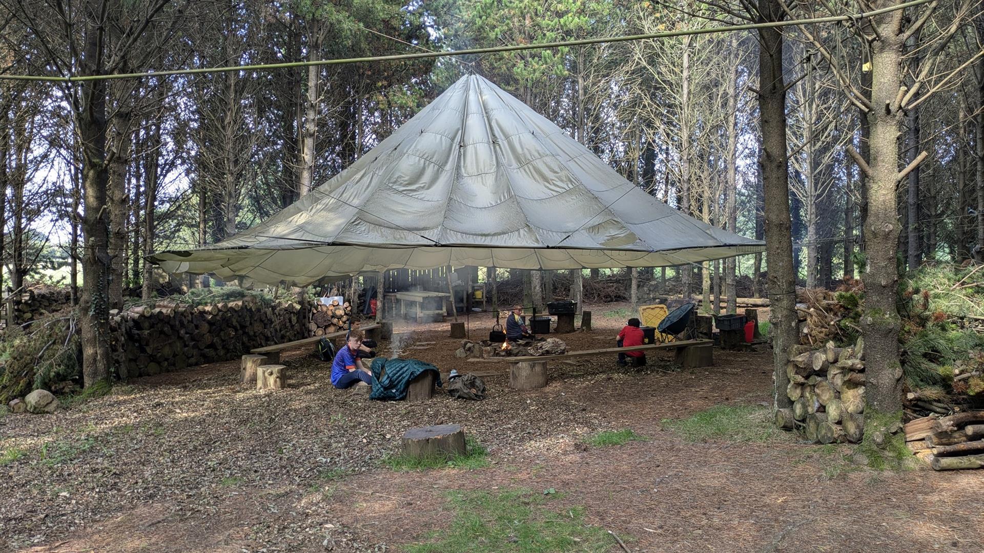 Men at Tepee in forest setting with campfire.