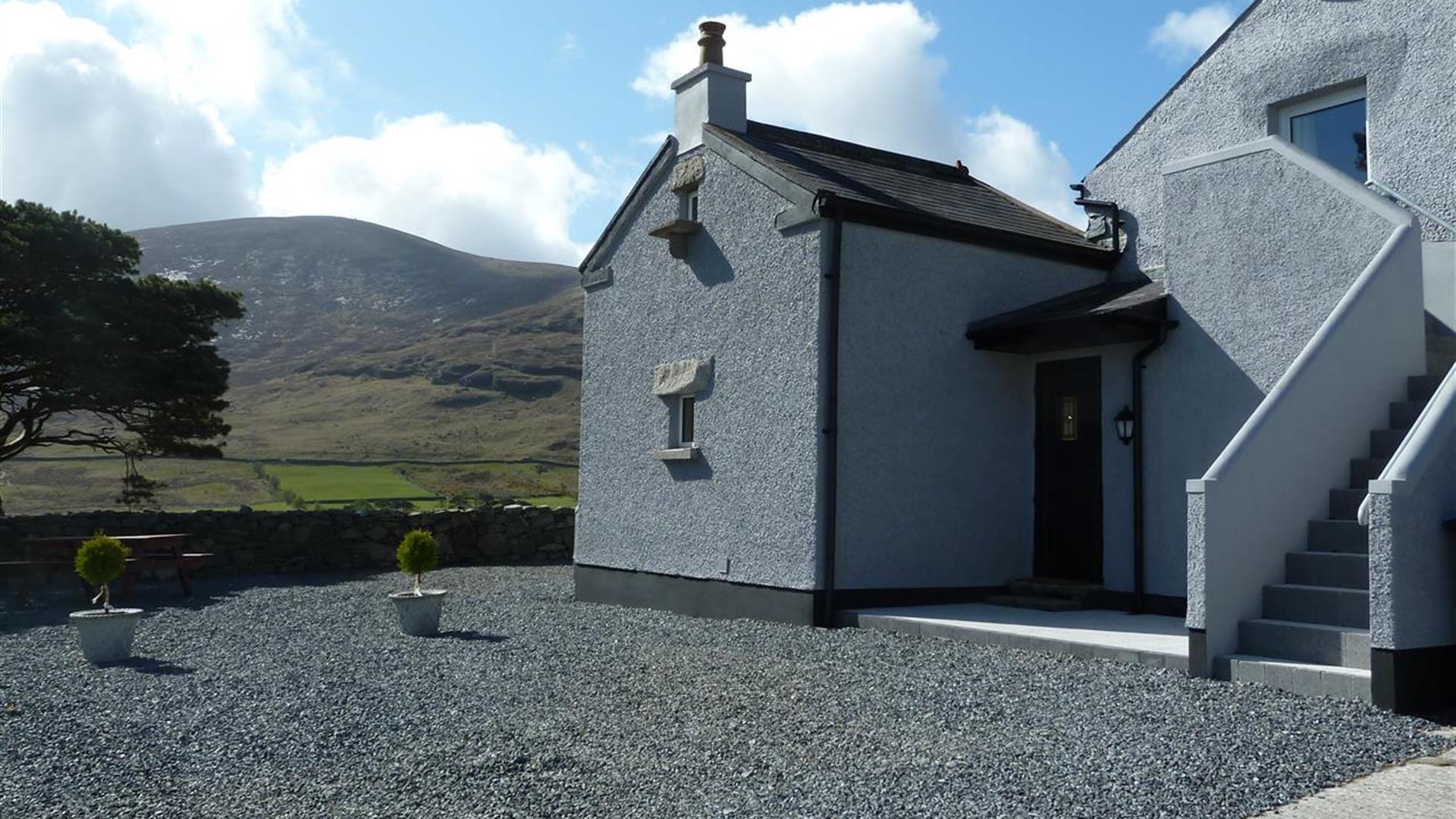 A large grey farmhouse with an exterior staircase in the mountains.