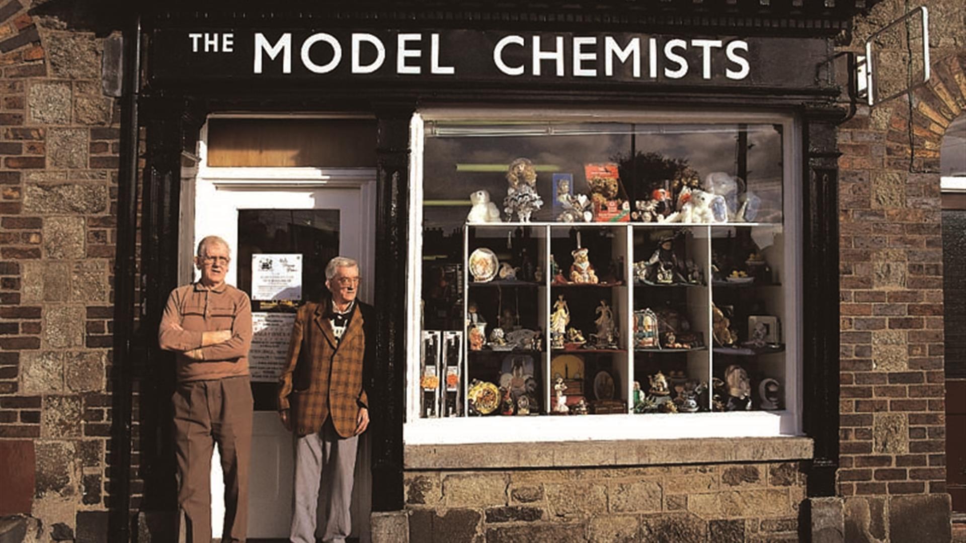 Two gentlemen standing outside 'The Model Chemist' building as part of the Bessbrook Historic Model Village