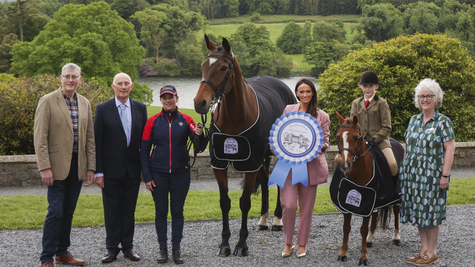 show organisers stand in front of castlewellan lake with a pony and a horse