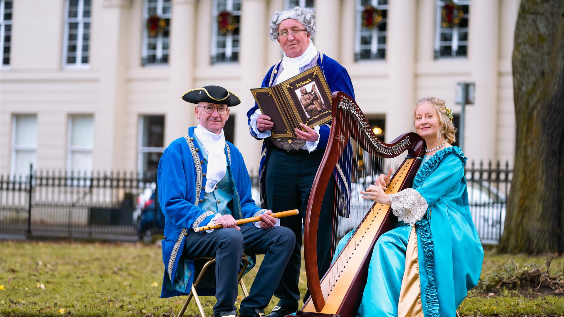 Three people in historical garments in front of a historical house.