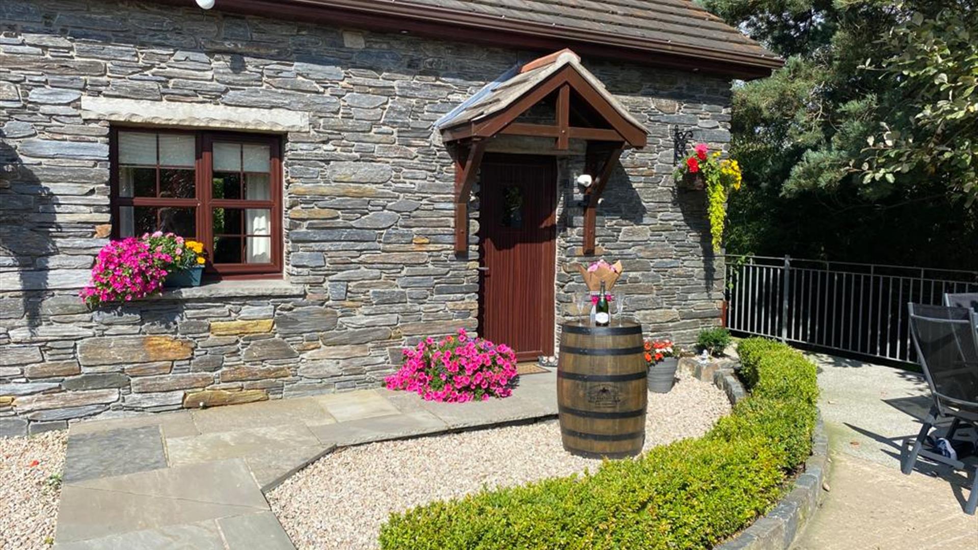 Front garden with paved path leading to the cottage's front door, decorated with flowers and a barrel.