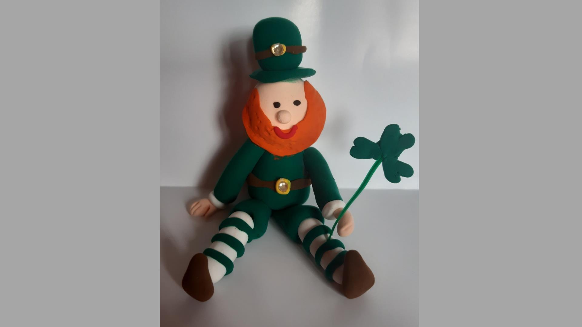 A handmade leprechaun with a shamrock in their hand, sitting on a table, on St Patrick's Day at Newry and Mourne Museum.