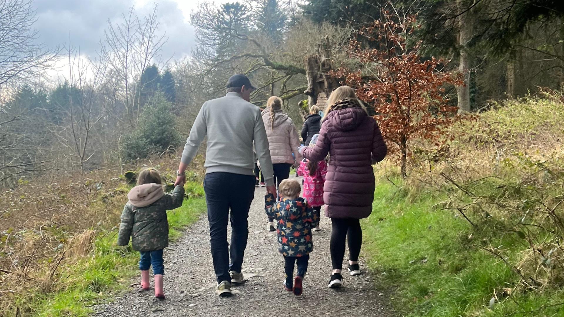 A family enjoying a walk in Slieve Gullion Forest Park. Two adults and two children holding hands, walking up a path together.