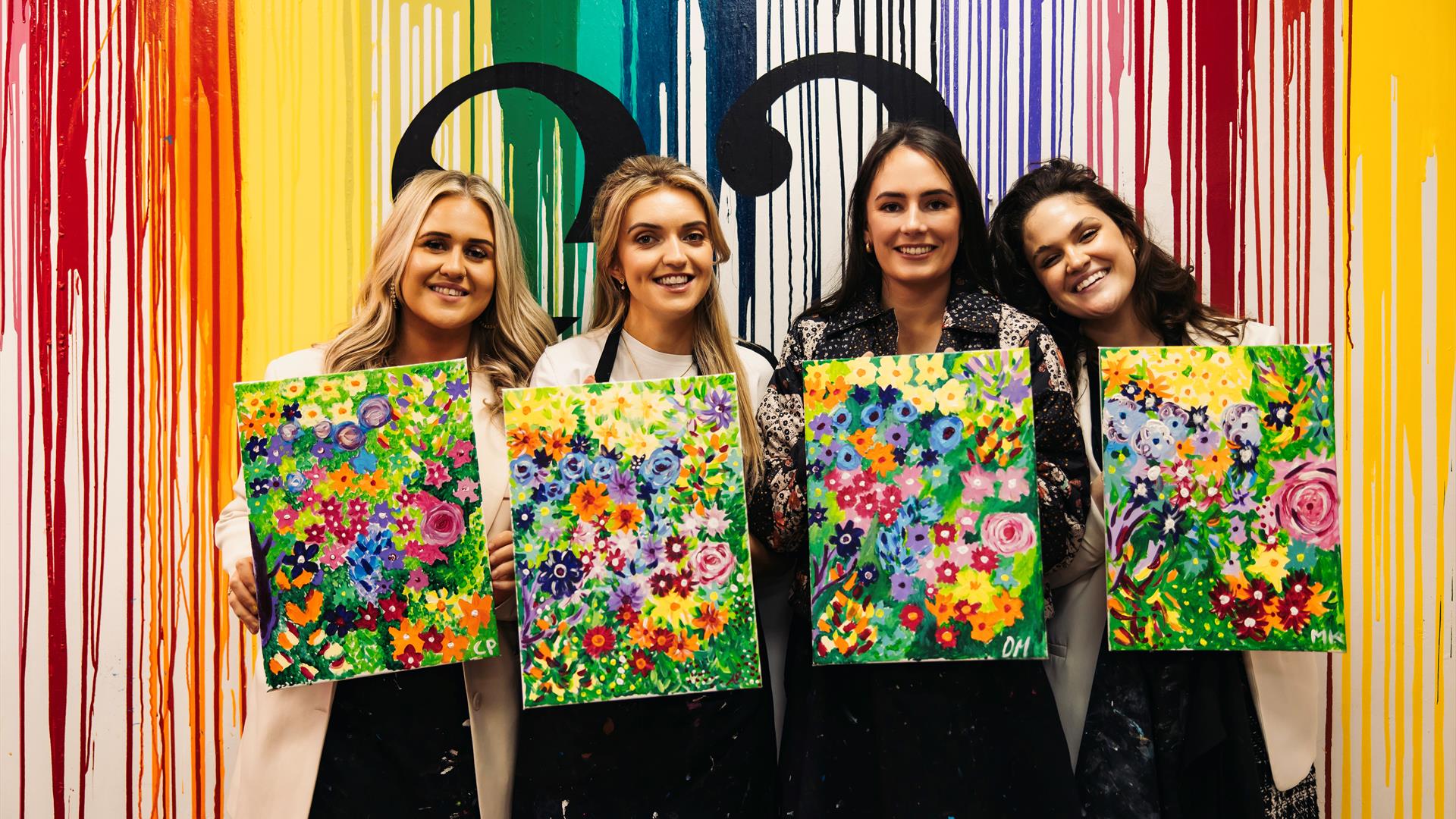 Image of group of girls holding paintings of flowers, painted in a class.